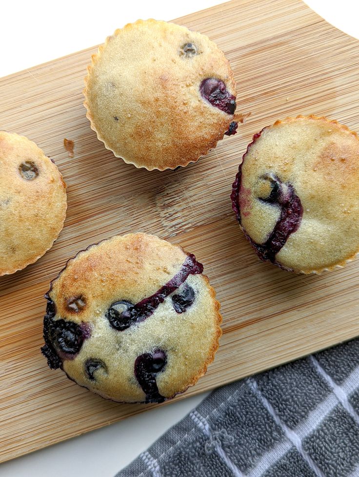 four blueberry muffins on a wooden cutting board