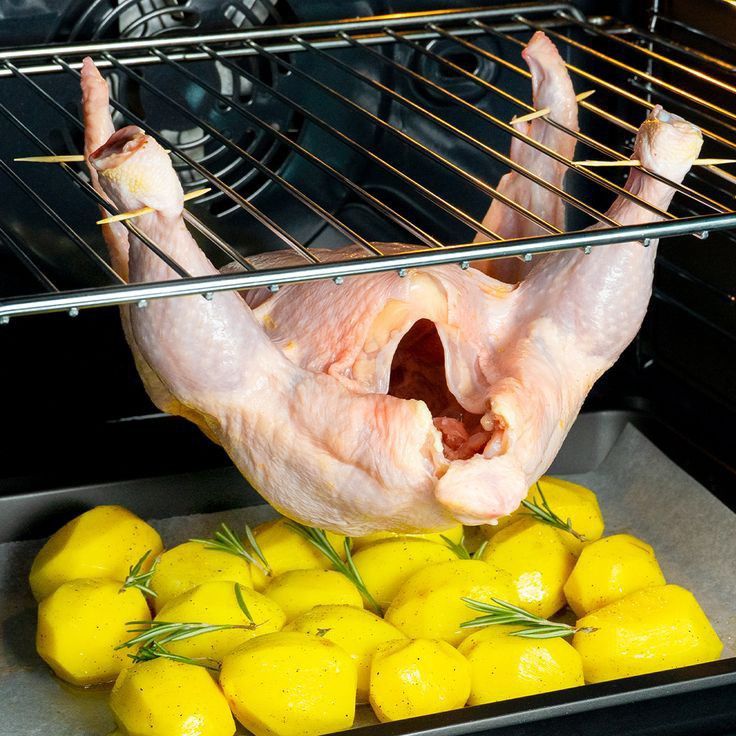 a raw chicken in the oven with lemons and rosemary sprigs next to it