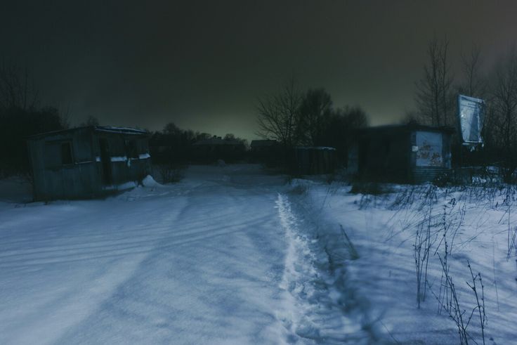 a snow covered road next to a shack in the woods at night with dark skies