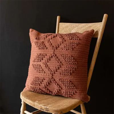 a brown pillow sitting on top of a wooden chair next to a black wall with a white frame