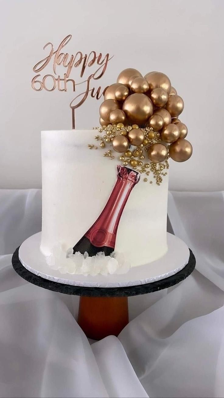 a white cake with gold decorations and a wine bottle on top