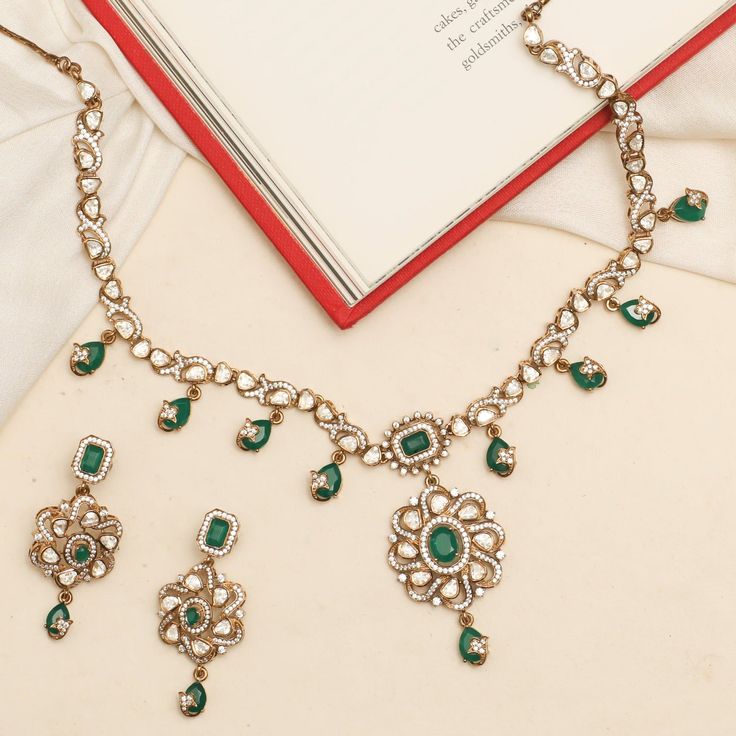 Description: Discover the Maya necklace set, a stunning blend of tradition and modern elegance. Showcasing a moissanite-studded central pendant with a floral design, highlighting an emerald green stone. Adorned with intricate motifs and drop emerald green stones, this necklace adds timeless brilliance and cultural charm to your jewelry collection. Product Information: Metal: 925 Silver with Victorian Plating Length: Necklace- 18cm, Earrings- 5cm Stones: High Grade CZ Stones Findings: Hook & Link Green Emerald Kundan Necklace With Gemstones, Emerald Necklace With Stone Work For Celebration, Festive Emerald Kundan Necklace With Intricate Design, Emerald Kundan Necklace With Intricate Design For Festive Occasions, Green Kundan Gemstone Jewelry Set, Kundan Jewelry Set With Green Gemstones, Traditional Green Emerald Necklace With Diamonds, Green Chandbali Jewelry For Formal Occasions, Hand Set Emerald Chandbali Necklaces