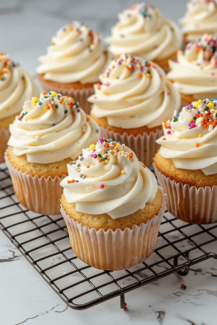 cupcakes with white frosting and sprinkles on a cooling rack