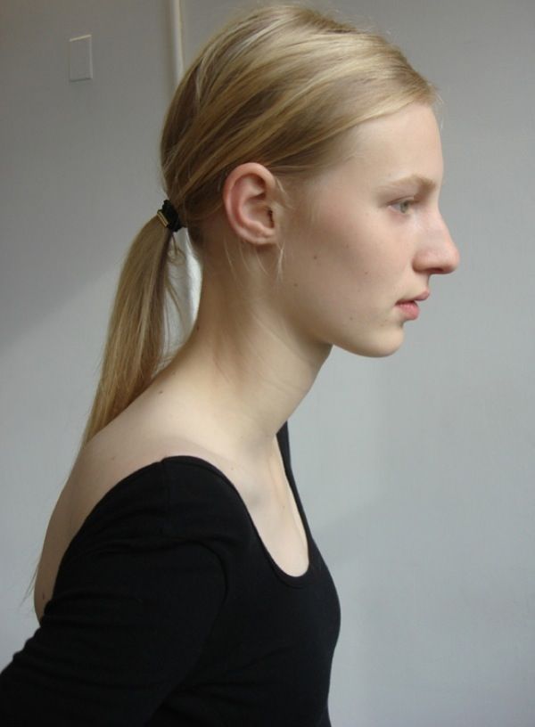 a woman with long blonde hair in a ponytail wearing a black shirt and looking off to the side