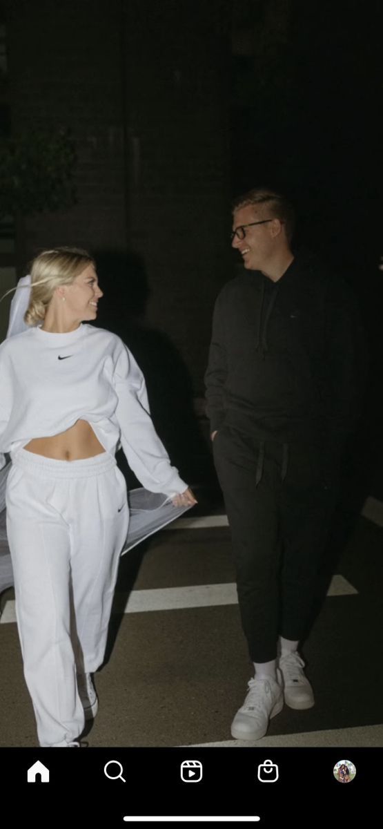 a man and woman walking down the street at night wearing white sweat suits with hoodies