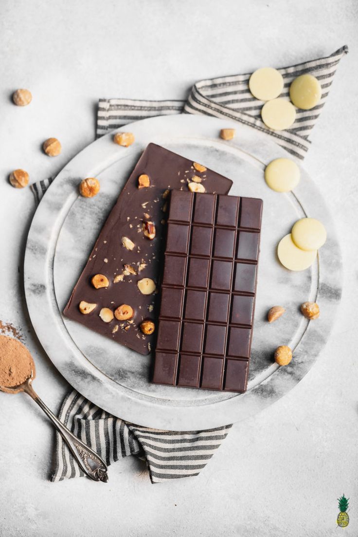 two pieces of chocolate sitting on top of a plate next to some nuts and spoons