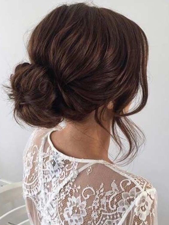 a woman with her hair in a low bun, wearing a white lace top and looking off to the side