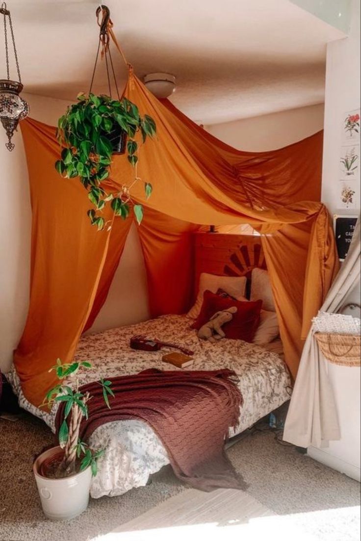 a bed with an orange canopy over it and some plants hanging from the ceiling above