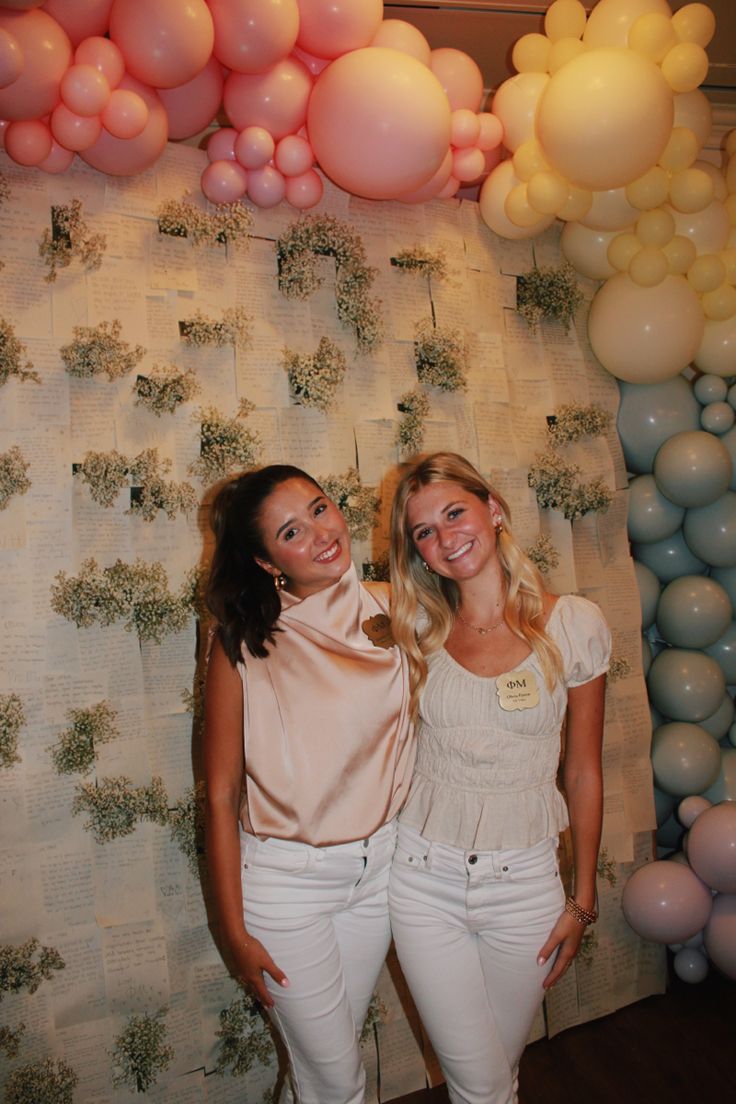 two beautiful young women standing next to each other in front of balloons and wall decorations