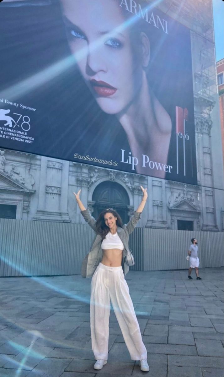 a woman standing in front of a large advertisement on the side of a building with her hands up