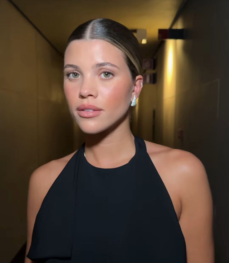 a woman in a black dress is posing for a photo with her hair pulled back