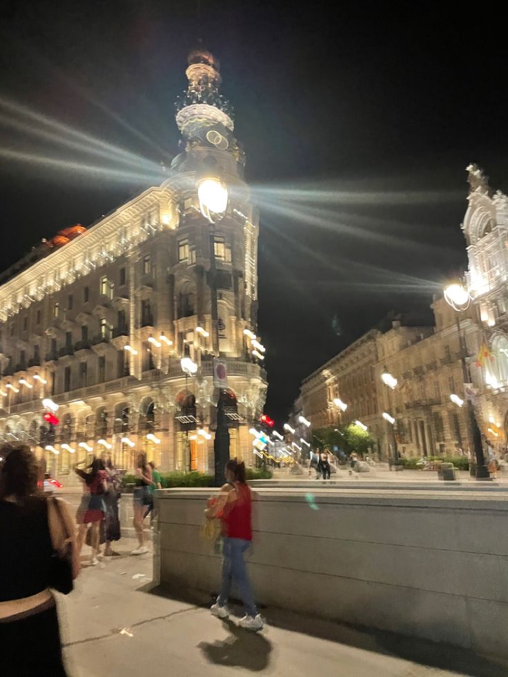 people walking and riding skateboards in front of a large building with lights on it