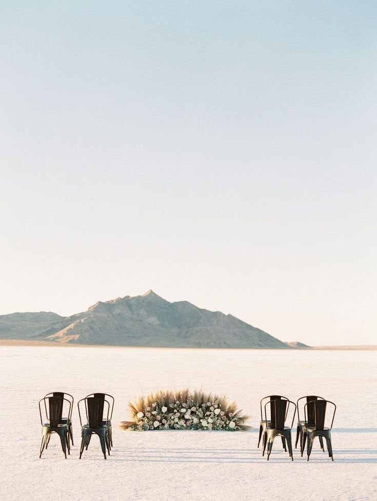 three chairs sitting in the middle of an empty field with a flower arrangement on it