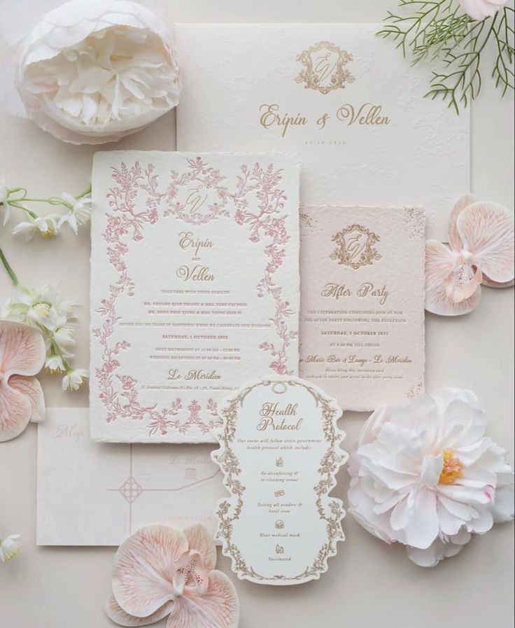 the wedding stationery is laid out with pink flowers and greenery on top of it