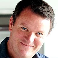 a close up of a person wearing a blue shirt and smiling at the camera with his eyes wide open