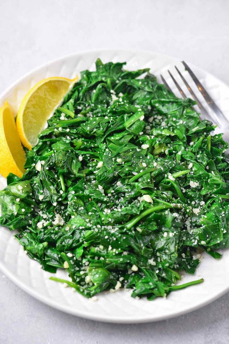 a white plate topped with spinach and lemon wedges next to a knife and fork