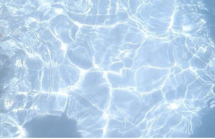 a person swimming in a pool with clear blue water and sun reflecting on the surface