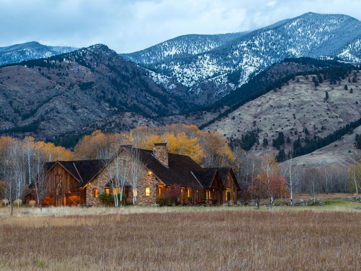 a large house in the middle of a field with mountains in the backgroud