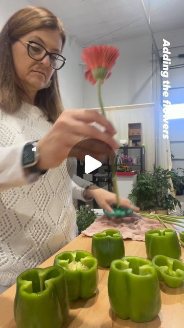 a woman is arranging green peppers on a table with a flower in the vases