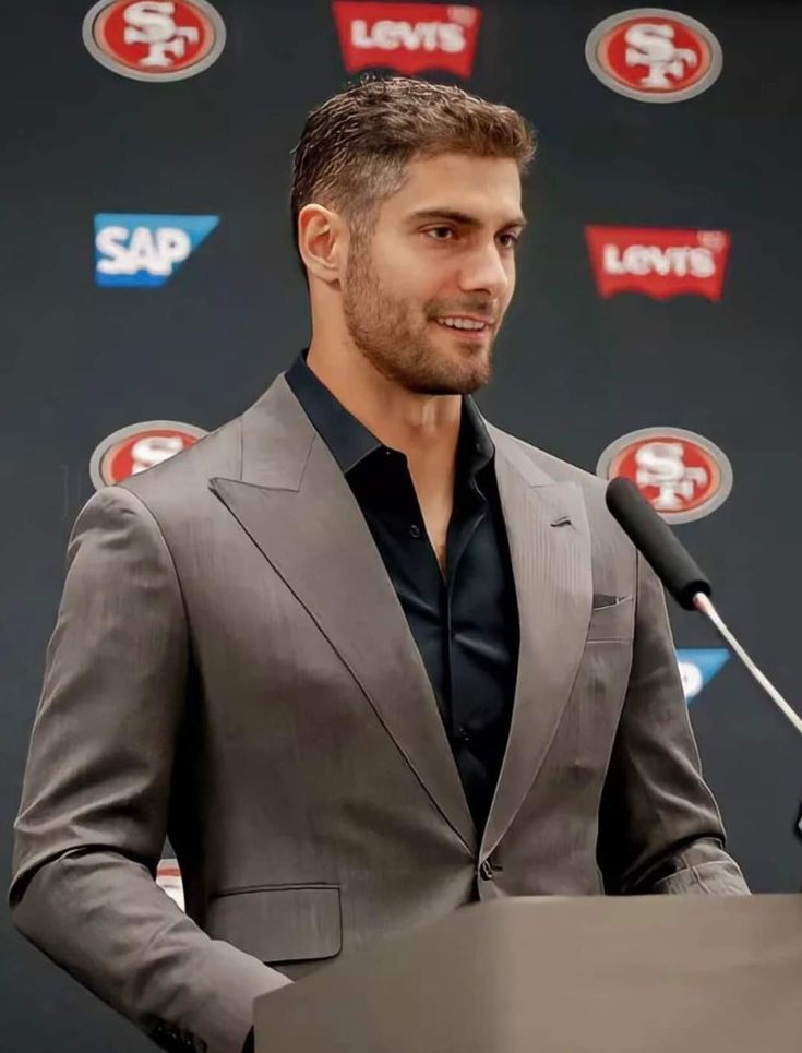 a man standing at a podium in front of a microphone with san francisco giants logos on the wall behind him