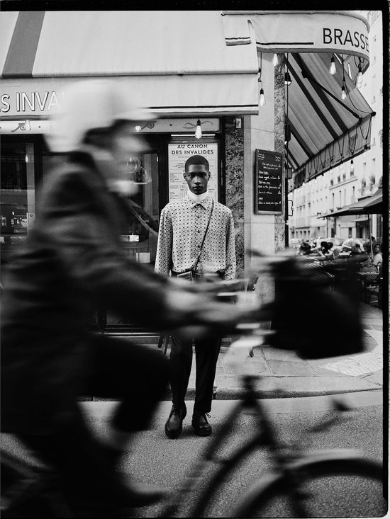 a black and white photo of a man standing in front of a store with his bike