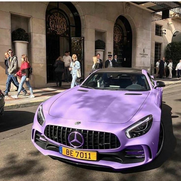 a purple mercedes sports car parked in front of a building with people walking around it