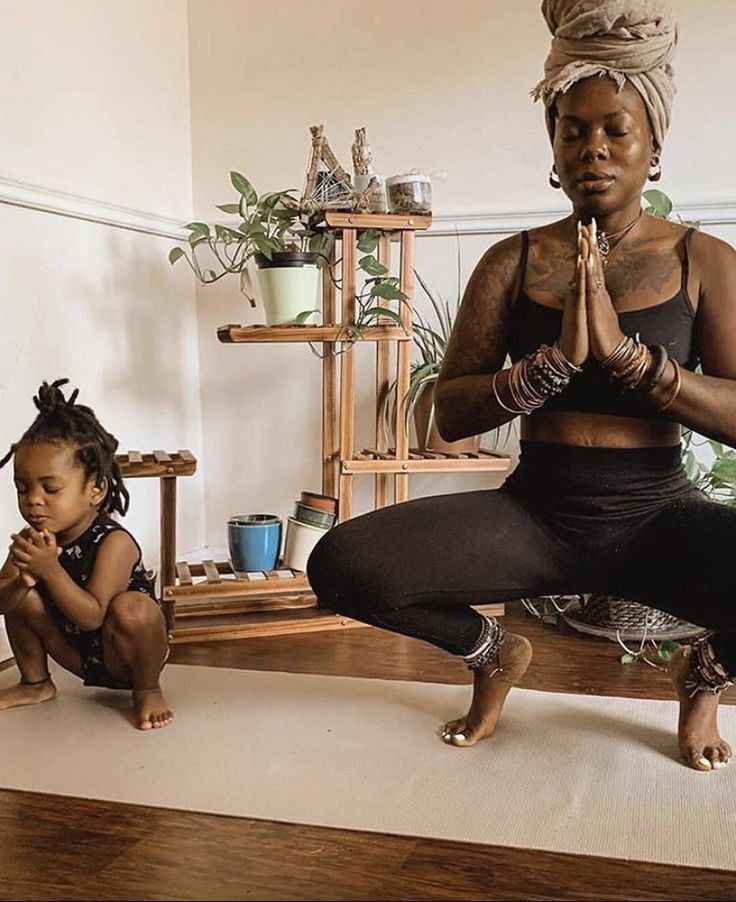 a woman sitting on the floor in front of a child who is kneeling down and doing yoga