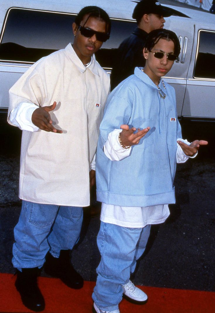 two men standing next to each other in front of a white car on a red carpet