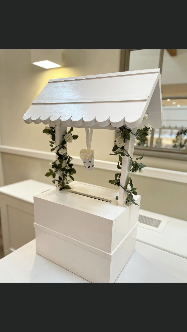 a white box sitting on top of a table covered in vines and ivys with a canopy over it