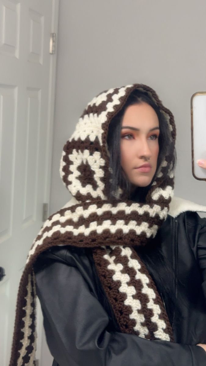 a woman wearing a brown and white crocheted scarf holding a cell phone in her hand