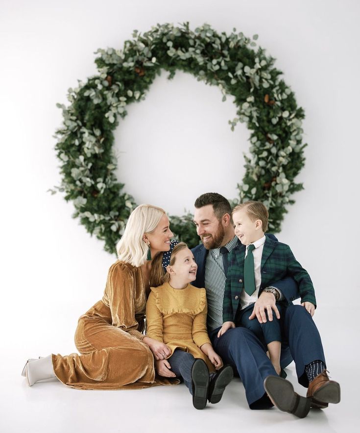 a family sitting in front of a christmas wreath