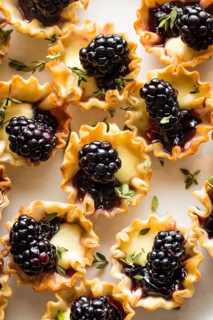 blackberries and cheese are arranged in small cups on a white platter with fresh herbs