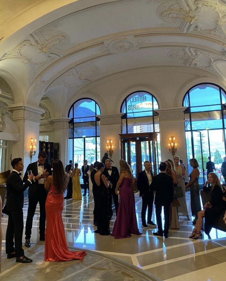 a group of people standing around in front of large windows at a formal event or function