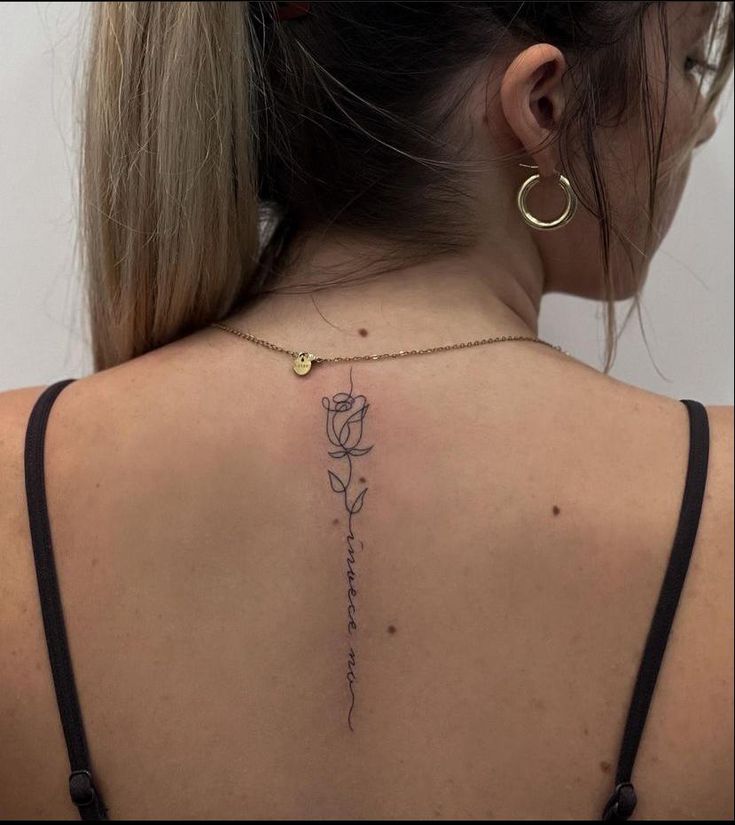 the back of a woman's neck with a rose tattoo on her left shoulder