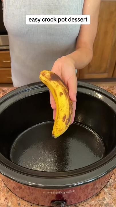 a person holding a banana over an empty crock pot