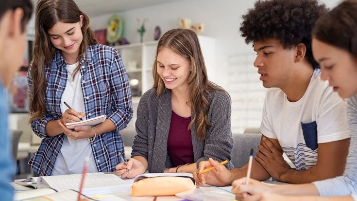 four young people sitting at a table with notebooks and pens in front of them