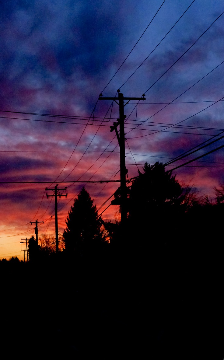 the sun is setting behind power lines and telephone poles with trees in the foreground