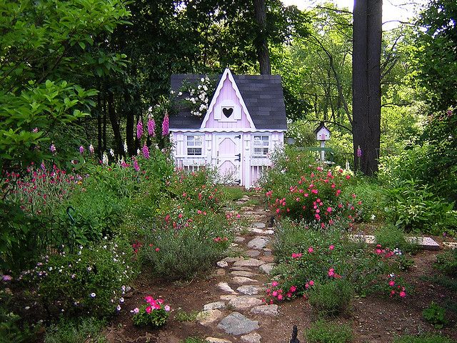 a small white house surrounded by trees and flowers with a stone path leading to it