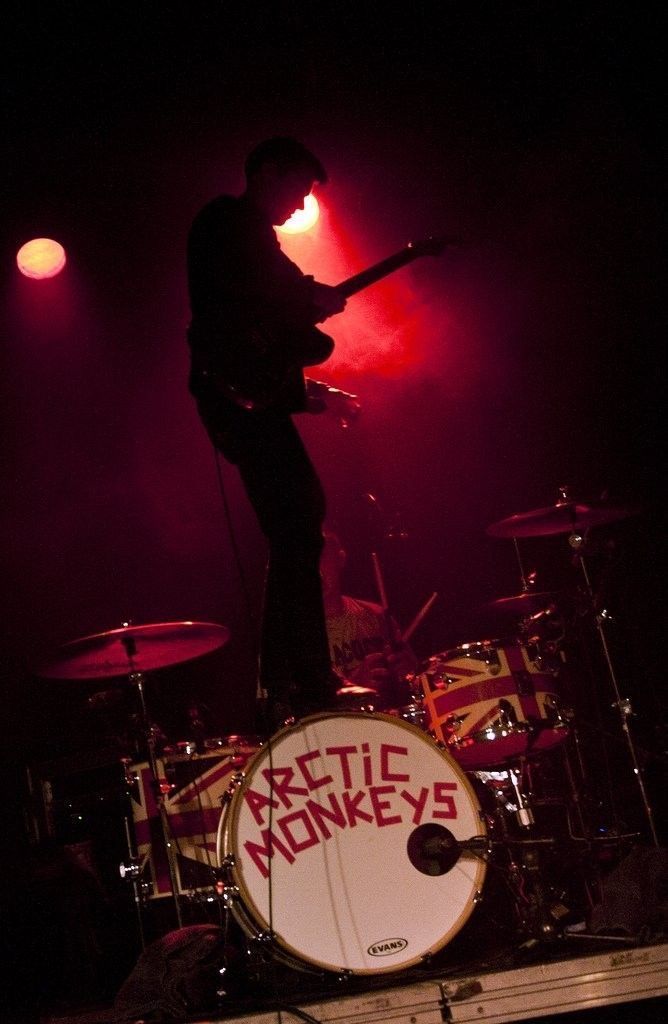 a man standing on top of a drum set in front of a red stage light