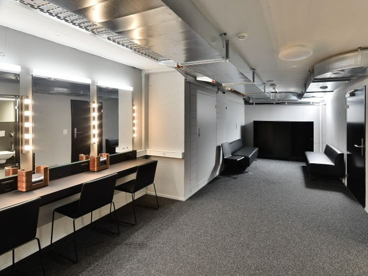 an empty dressing room with mirrors and lights on the wall, along with black chairs