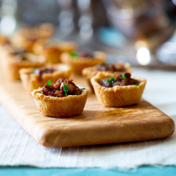 small tarts are lined up on a wooden cutting board, ready to be eaten