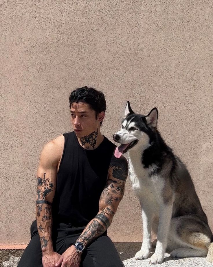 a man sitting on the ground next to a husky dog