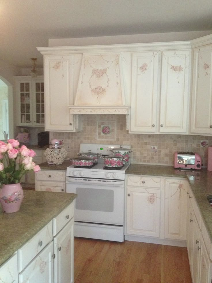 a kitchen with white cabinets and pink flowers on the counter top, in front of an oven