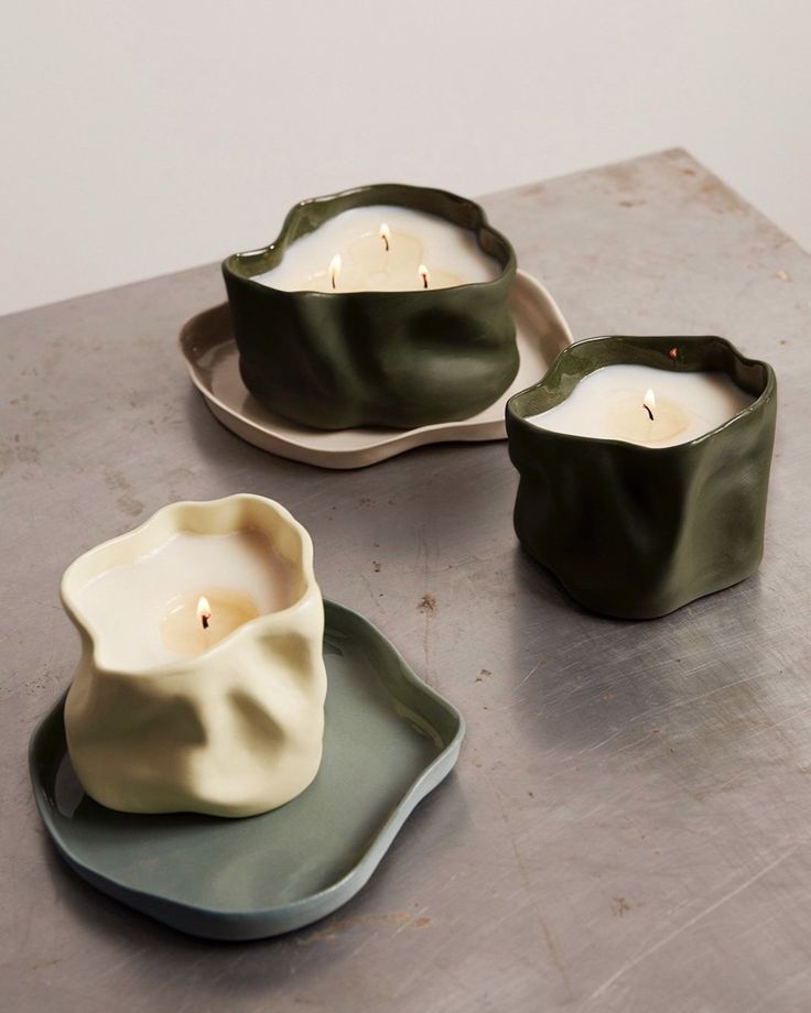 two green and white dishes with candles in them sitting on a table next to each other