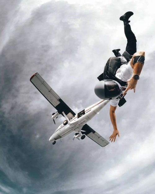 a man flying through the air while riding on top of a jetliner under a cloudy blue sky