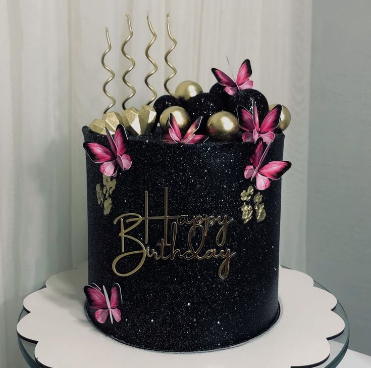 a black and gold birthday cake with pink butterflies