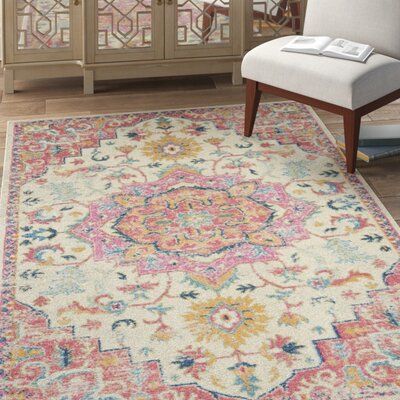 an ornate rug with pink, yellow and blue colors on the floor next to a white chair