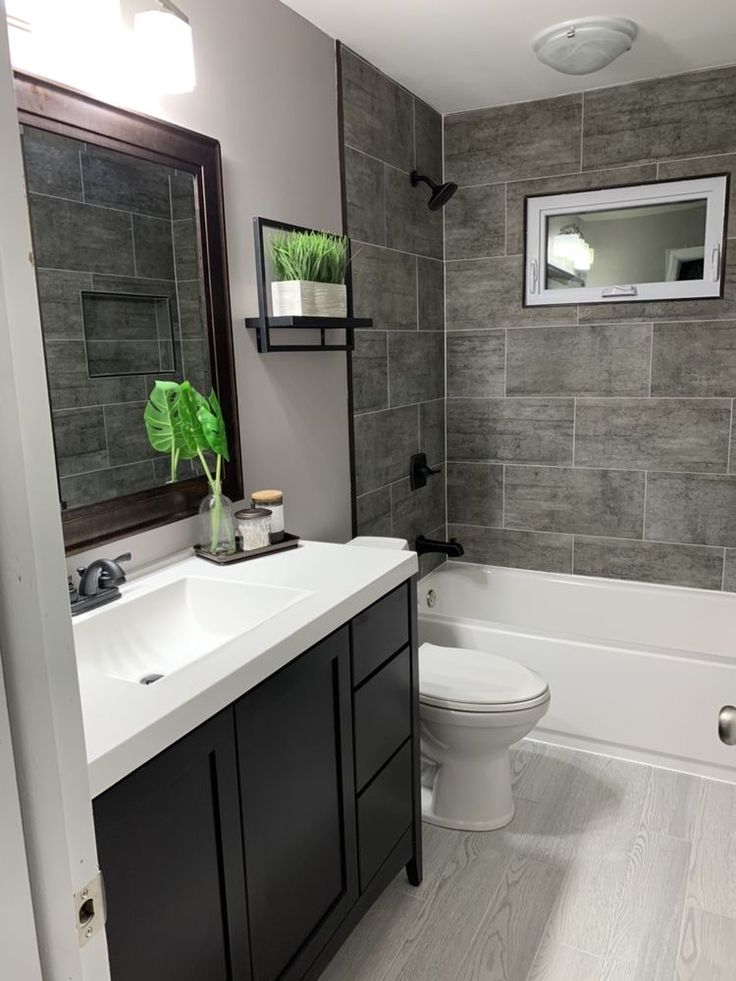 a white toilet sitting next to a bath tub in a bathroom under a window with a mirror above it