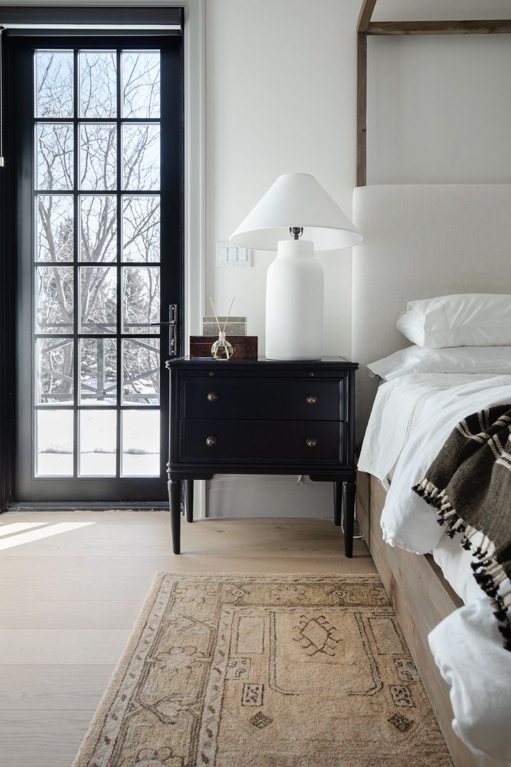 a bed sitting next to a black dresser on top of a wooden floor near a window