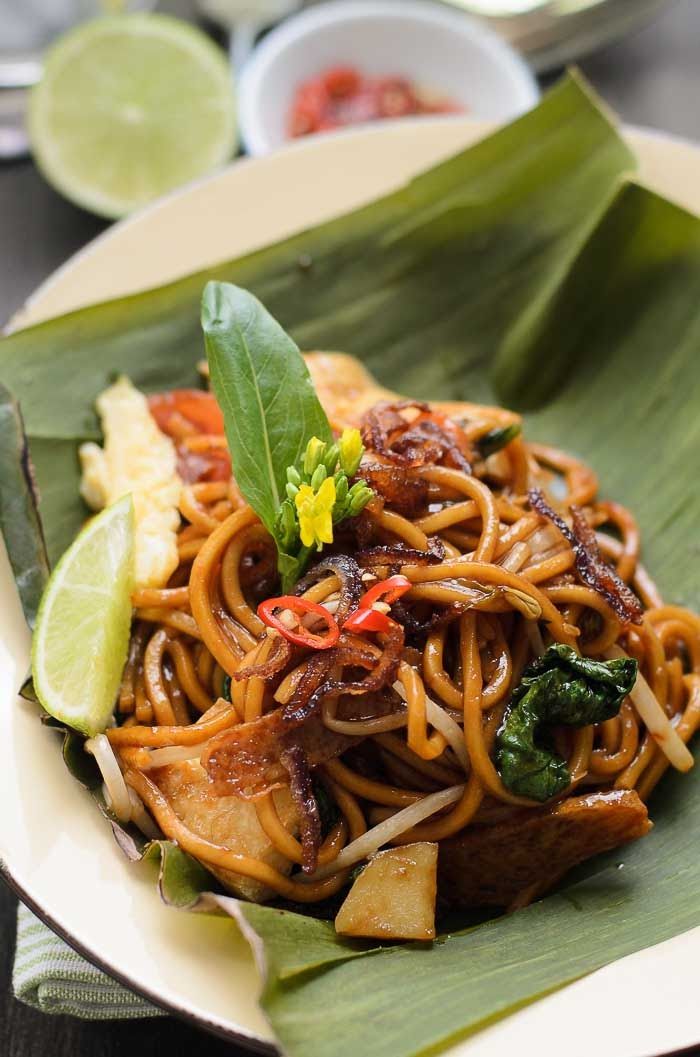 a plate filled with noodles and vegetables on top of a leafy green plate next to other plates